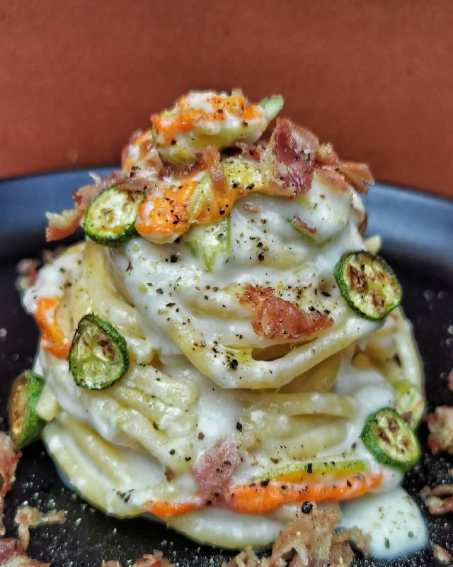 Bigoli gourmet con crema di pecorino, zucchine croccanti, fiori di zucca e petali di guanciale croccante